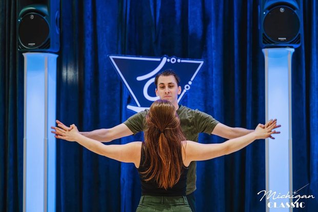 Ben and his partner mid-routine, arms extended, in front of a blue curtain